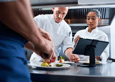 A kitchen team plating beside a live ticket display